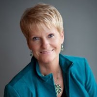 Smiling person in teal jacket, short hair.