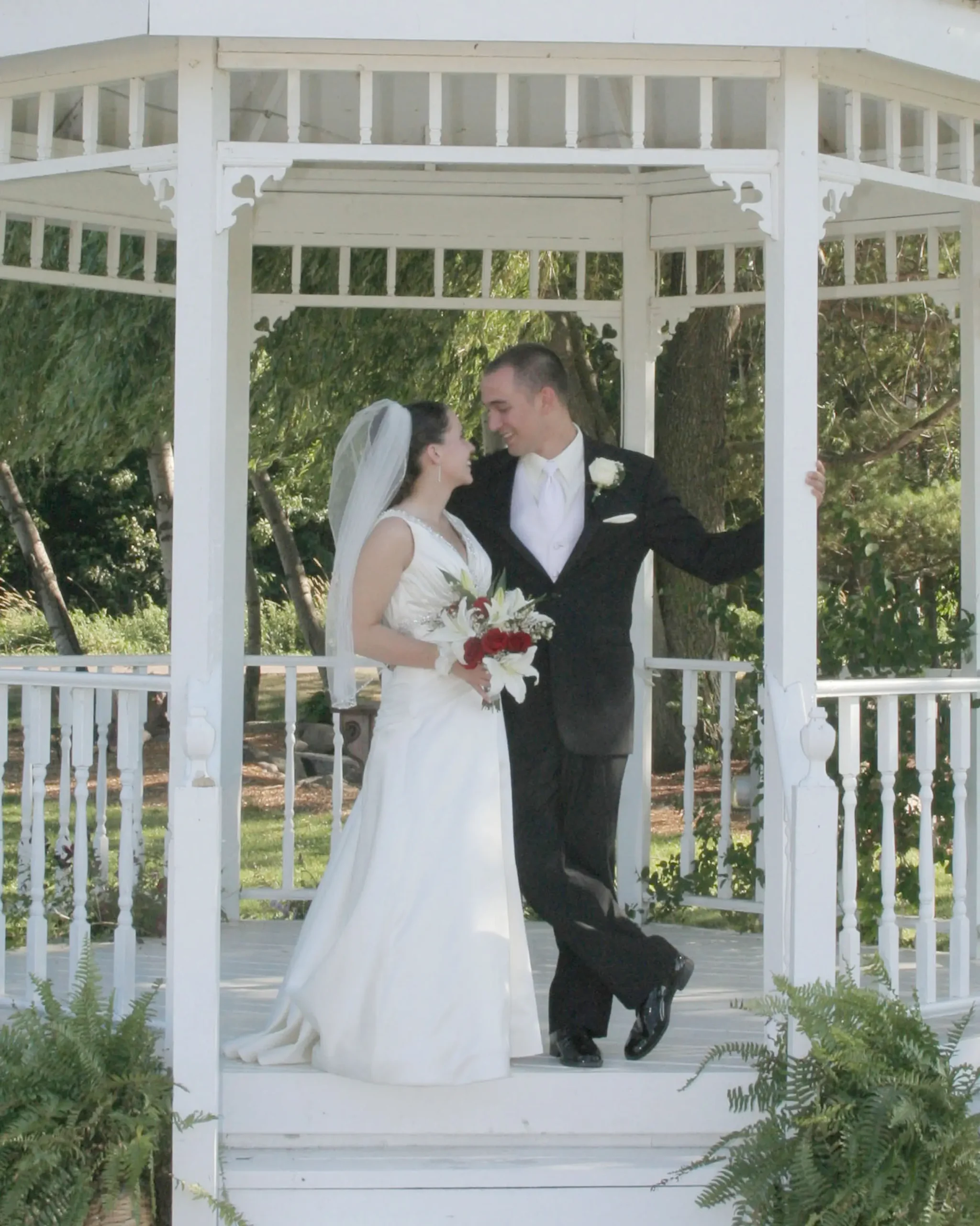 Bride and groom posing under a white gazebo on their wedding day.