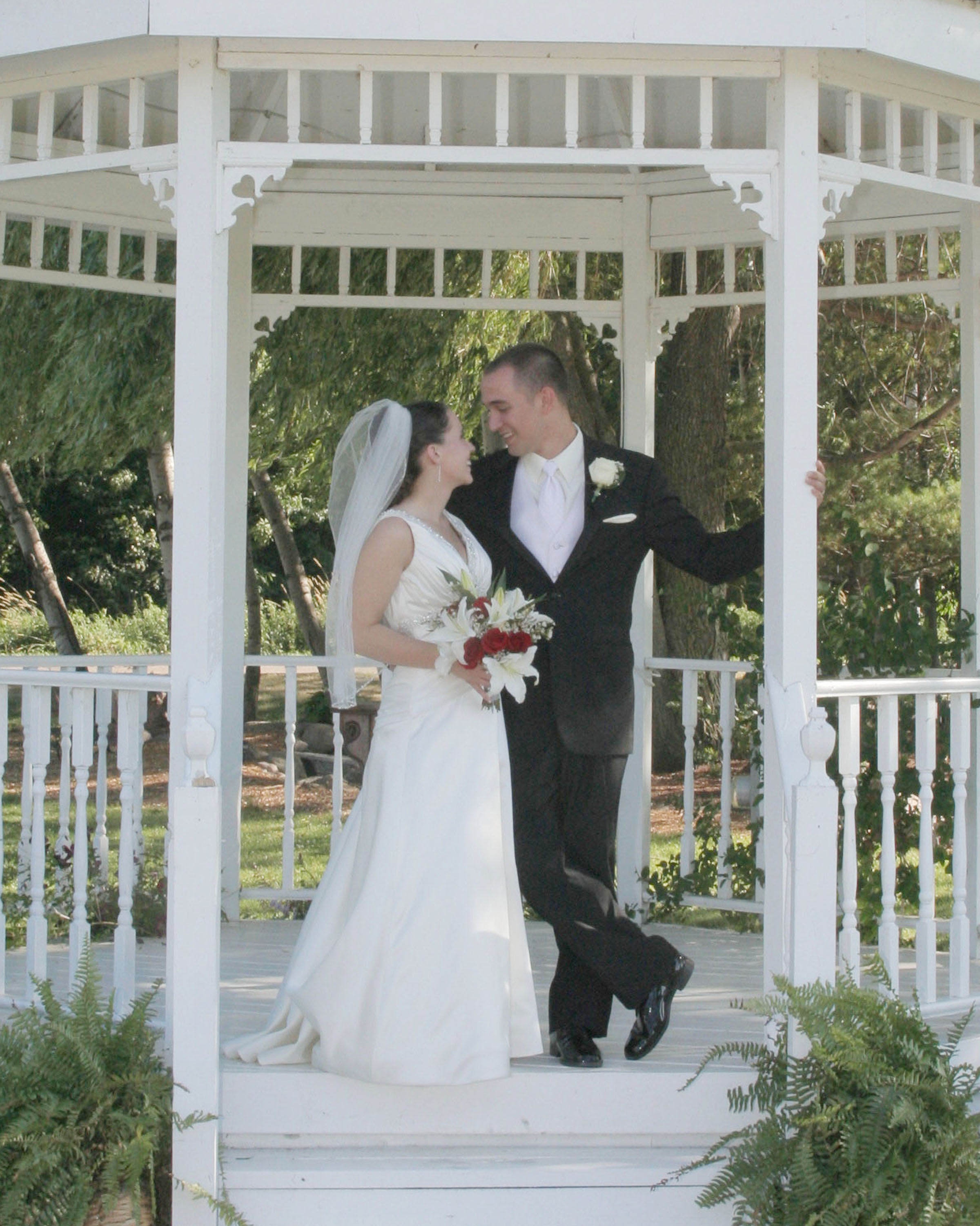 Bride and groom posing under a white gazebo on their wedding day.