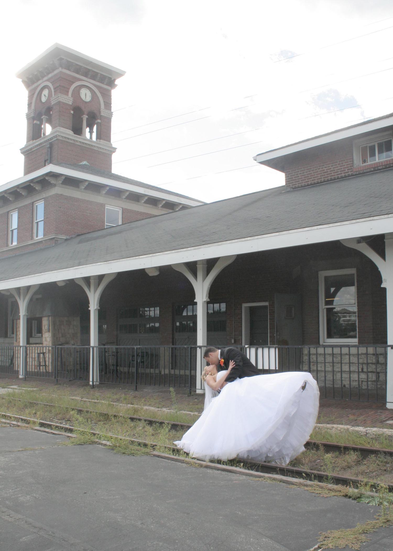 Bride and groom posing by a rustic train station platform.