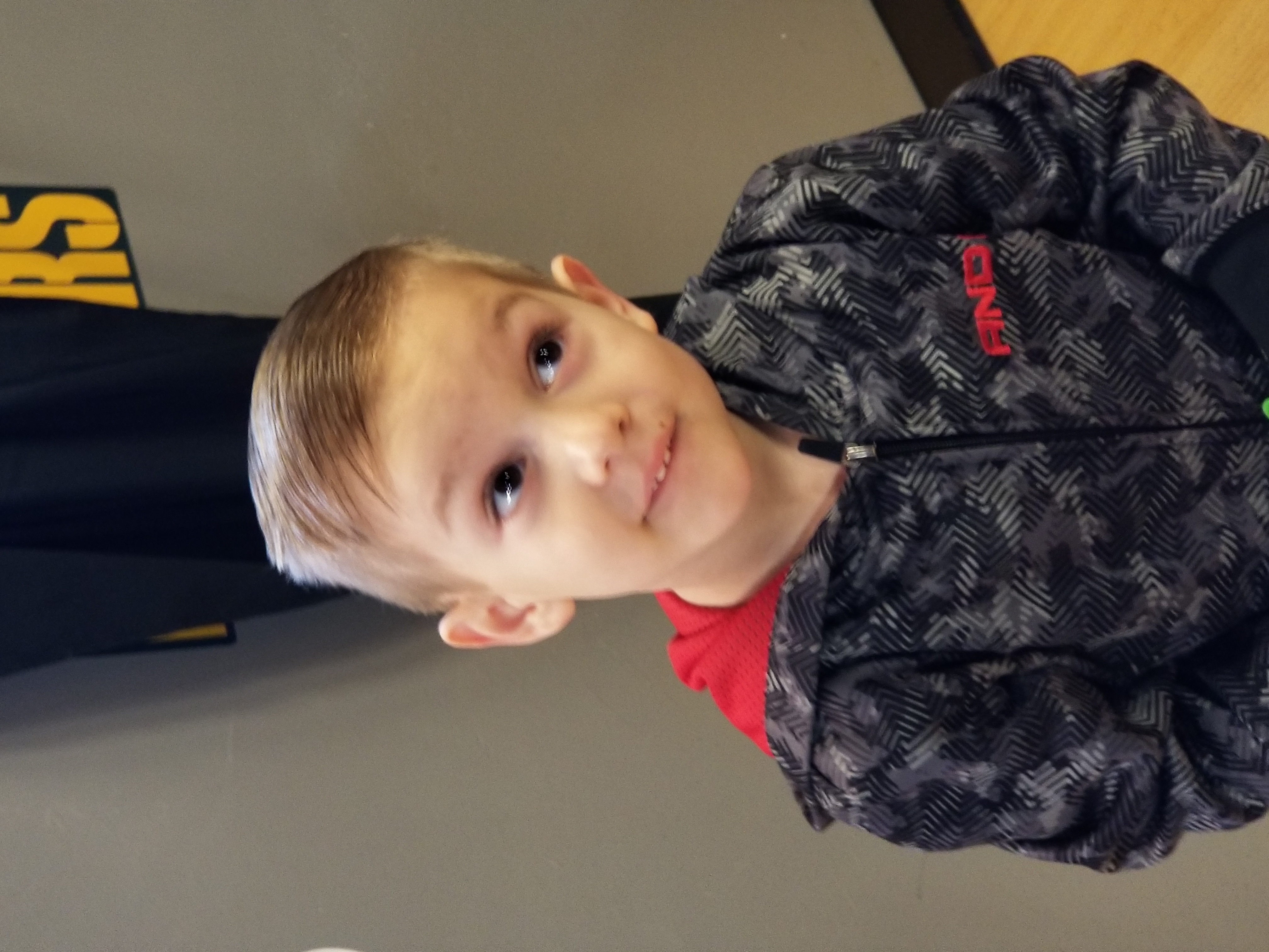 A young boy with light brown hair wearing a dark hoodie looking to the side.