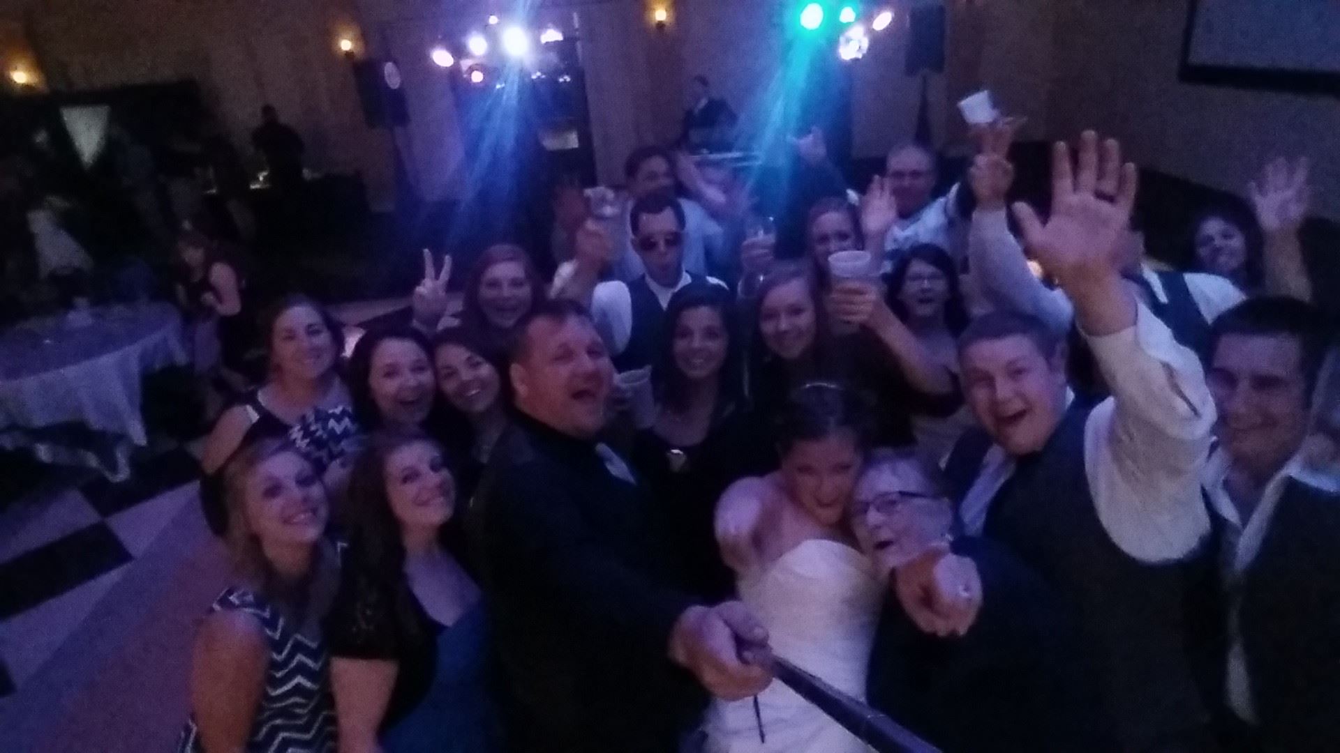 Group selfie at a lively party with smiling people and colorful lights.