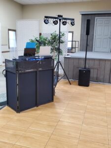 Indoor DJ setup with lighting and speakers near a small stage.