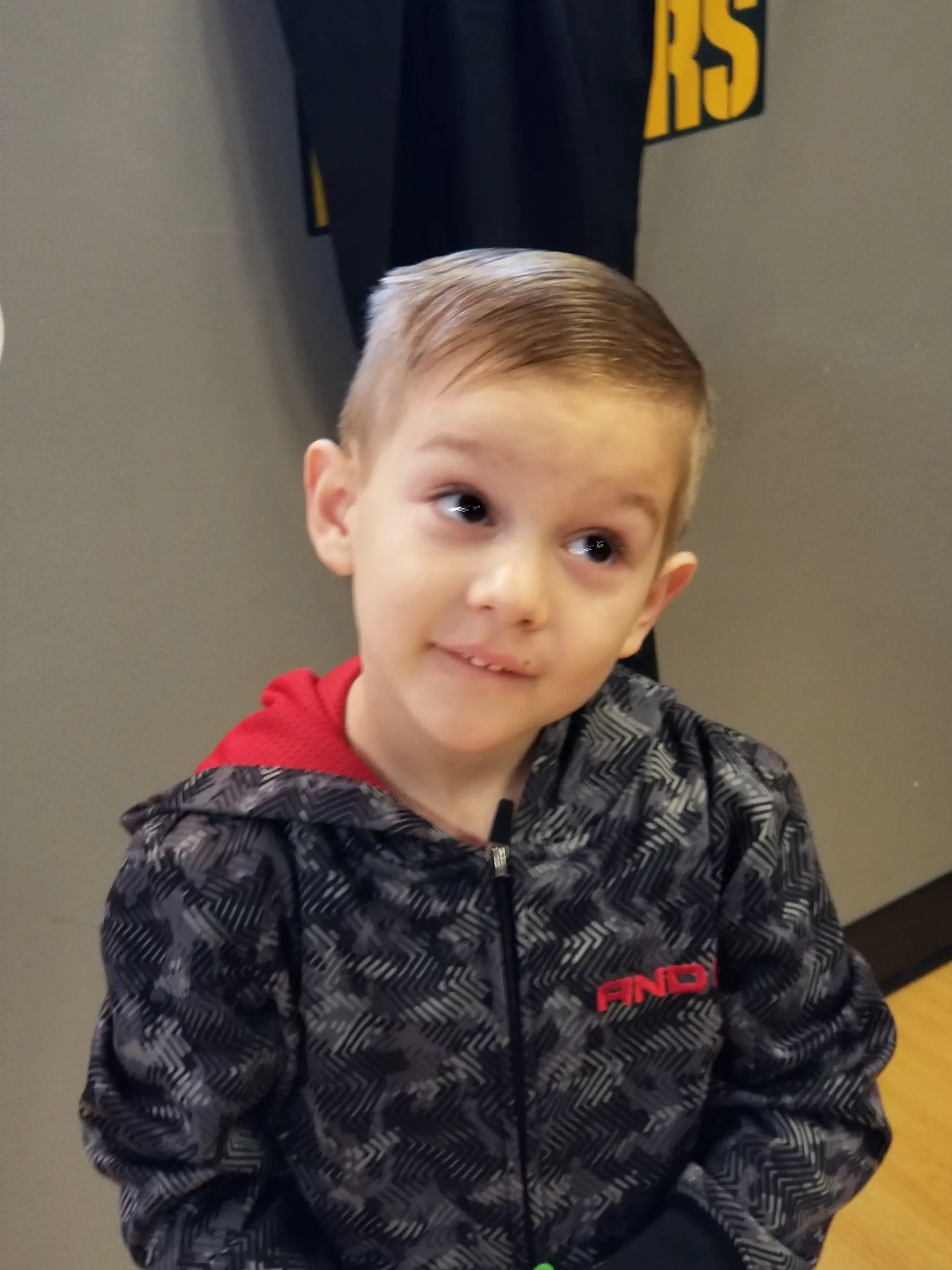 A young boy with light brown hair wearing a dark hoodie looking to the side.